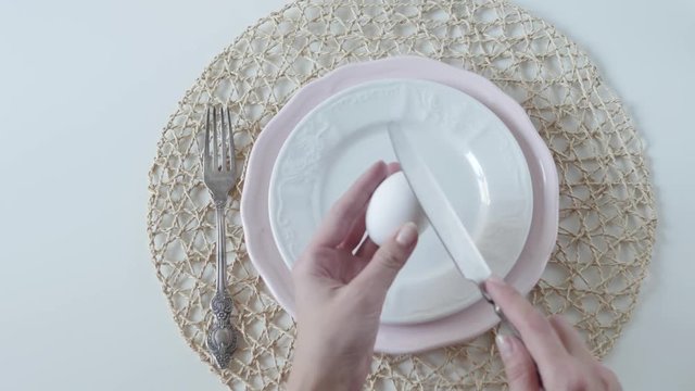 table setting with white dishes on white background. boiled egg for breakfast. female hands lay an egg in a plate.