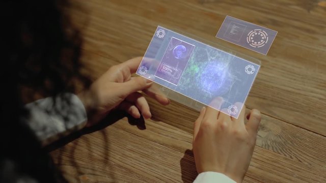Unrecognizable woman working on a futuristic tablet with a hologram text Develop. Women's hands with future holographic technology at a wooden table
