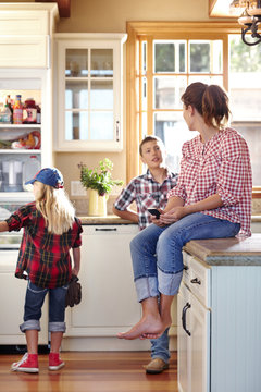 Mom and two kids hanging in kitchen with little girl looking inside fridge