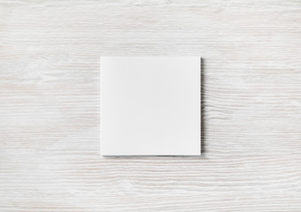 Blank square notebook on light wooden background. White paper notepad. Flat lay.