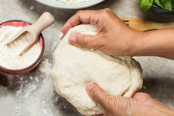 Manos de mujer sosteniendo un bollo de masa crudo sobre una mesa gris en la cocina. Vista superior...