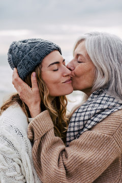 Senior woman kissing her daughter on the beach.