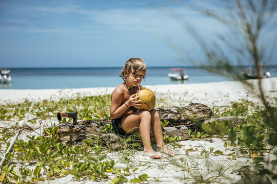 cute little boy drinking fresh coconut juice on white sand beach - Powered by Adobe