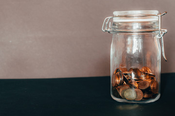 Closed clear glass jar with rubber lid and metal clamp half full with small coins an a grey background – Concept image for savings, investment, good wealth and financial education