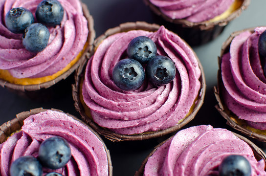 Set of cupcakes with blueberry cream decorated with fresh blueberries on black plate