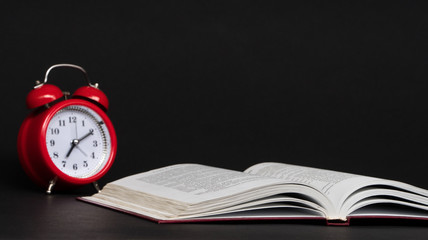 red alarm clock and open book on black background, isolated. back to school