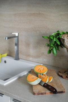 Cut cantaloupe on a cutting board with a knife next to the sink in the modern kitchen