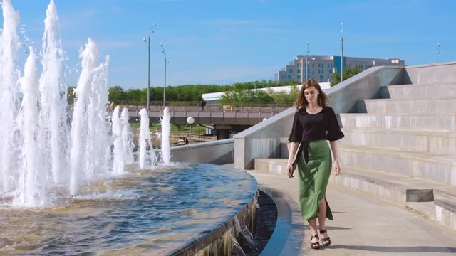Girl walking along the fountain in summer sunny day