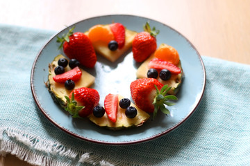 Various spring fruit on a turquoise plate: strawberries, pineapple, blueberries and tangerine. Selective focus.