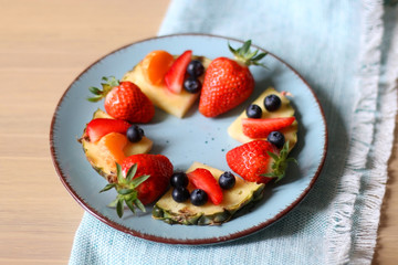 Various spring fruit on a turquoise plate: strawberries, pineapple, blueberries and tangerine. Selective focus.
