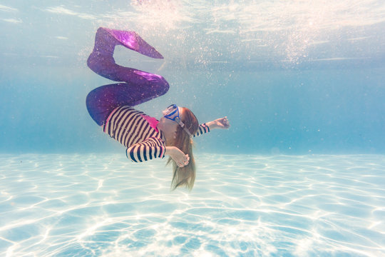 Girl on family vacation spins gracefully in swimming pool wearing mermaid costume