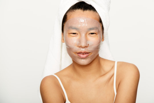 Young asian woman smiling with facial gel mask on during skincare treatment
