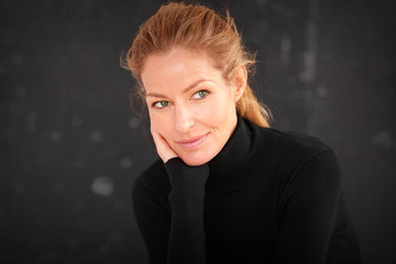 Fototapeta premium Attractive blond haired woman wearing roll neck sweater and thinking while sitting at dark background