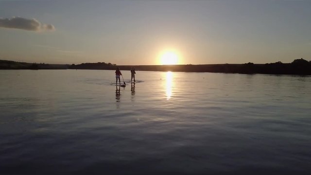 Drone arieal scene with couple practicing stand up surf at beautiful sunset