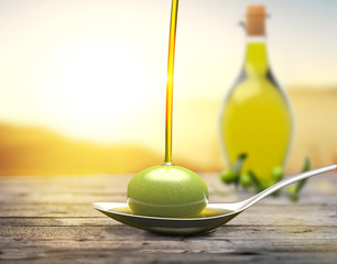 A spoon with an olive under a fall of olive oil