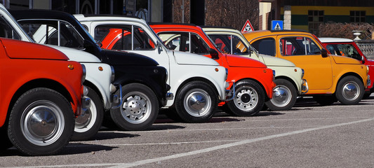  A row of colorful vintage Fiat 500 s  in a roadside parking lot on a sunny day. - obrazy, fototapety, plakaty
