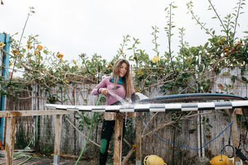 Woman washing surfboard in backyard