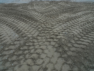 Heavy machines tracks in the sand.  During road work, heavy machines go back and forth. The crisscross  pattern they leave on the ground is quite interesting.