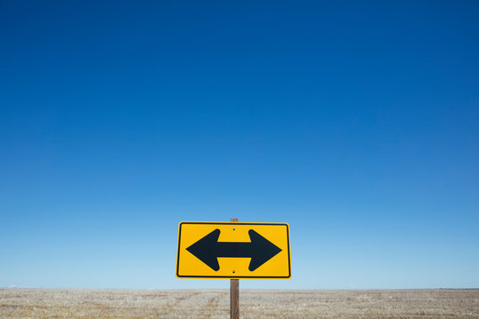 Naklejki Arrow road sign, rural farmland in background