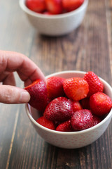 Man's hand picking a strawberry from a bowl of strawberries on wooden background