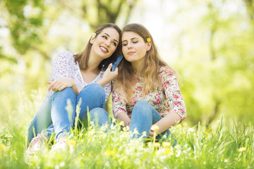 Two young women sitting outdoors and using phone