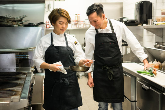 Two Chefs Look Over A Dish Together As They Prep It