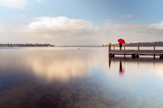 Girl with a red umbrella on a jetty over a smooth water