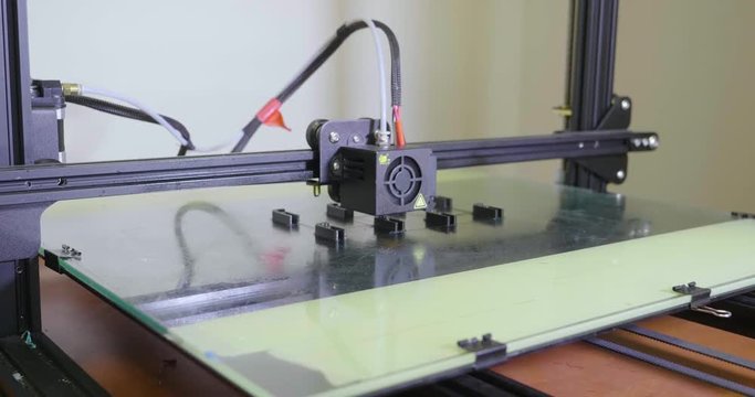 Panning left shot across automation process of 3D printer creating small geometric component parts in repetition on flat bed technology design.