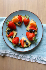 Various spring fruit on a turquoise plate: strawberries, pineapple, blueberries and tangerine. Top view.