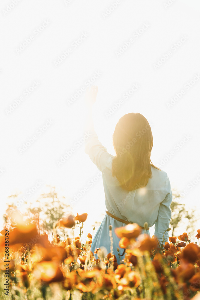 Sticker Romantic woman waving to the sun in flower meadow.