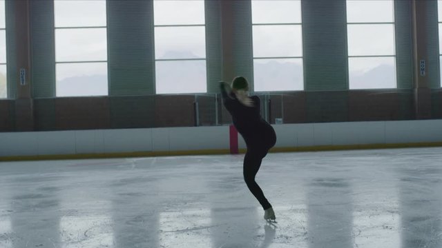 Slow motion of woman figure skating on ice skating rink while holding leg raised / Murray, Utah, United States