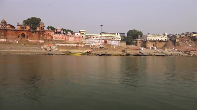 Wide low-angle dolly shot of the old Chet Singh and Niranjani Ghats, and anchored boats along the river bank, River Ganges