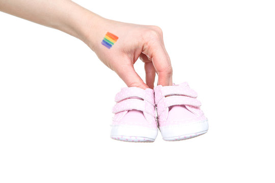 Female hand with drawing rainbow flag and baby shoes on white background