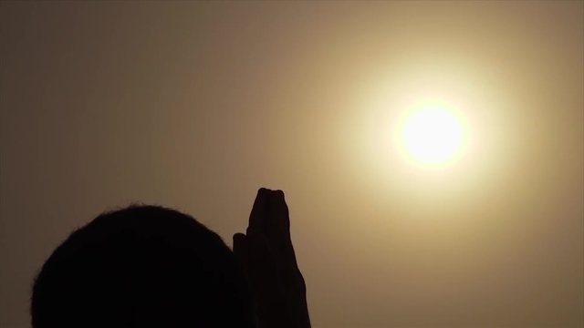 Wide low-angle still shot of a the setting sun, and a silhouette portrait of Hindu devotee in a lotus position during sunset meditation, Ganges