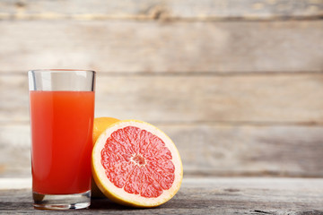 Ripe grapefruits and glass of juice on grey wooden table