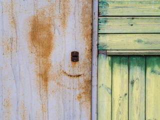 on the left, a part of an old metal door with a rusty keyhole, on the right a wooden wall of narrow vertical and horizontal planks of green color