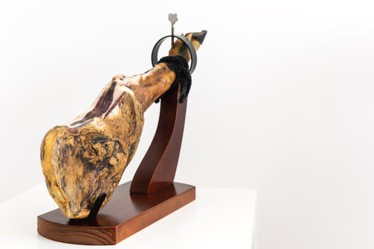 Spanish delicatessen dry cured meat ham, whole leg, jamon iberico bellota on jamonero stand selective focus - white background