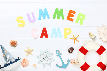 Paper text Summer camp with seashells, lifebuoy and decorative ship on white wooden table