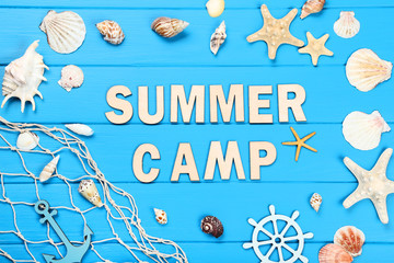 Text Summer camp with seashells and fishing net on blue wooden table