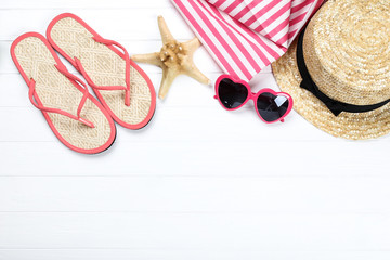 Pair of flip flops with starfish, sunglasses and hat on white wooden table