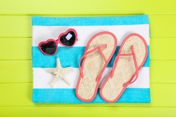 Fototapeta premium Pair of flip flops with starfish, towel and sunglasses on green wooden table