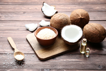 Coconuts with oil in bottles and flakes on brown wooden table