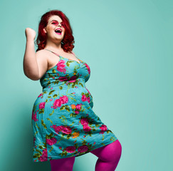 Happy plus-size lady overweight woman in fashion sunglasses and colorful clothes shows Yes sign...