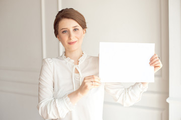 young smiling woman holding a blank sheet of paper for advertising.Girl showing banner with copy space.