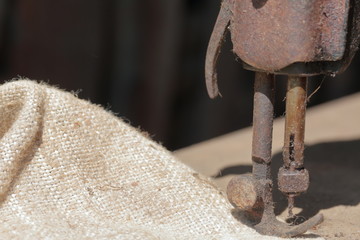 Old sewing machine, with manual drive. Covered with corrosion, dust and cobwebs. A piece of coarse fabric is sewn into it.