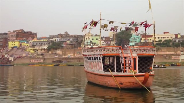 Wide, low-angle dolly shot of Vijayanagaram Ghat
behind a sailing pink decked passenger boat,  Ganga River, Varanasi, India