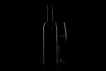 Elegant red wine glass and a wine bottle over black background