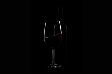 Elegant red wine glass and a wine bottle over black background