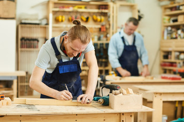 Portrait of two carpenters working with wood standing at tables in workshop, copy space