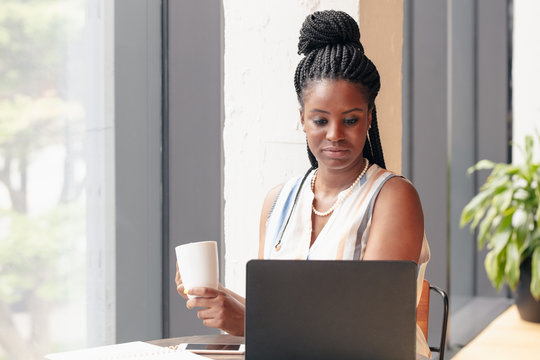 Businesswoman holds mug while looking at laptop